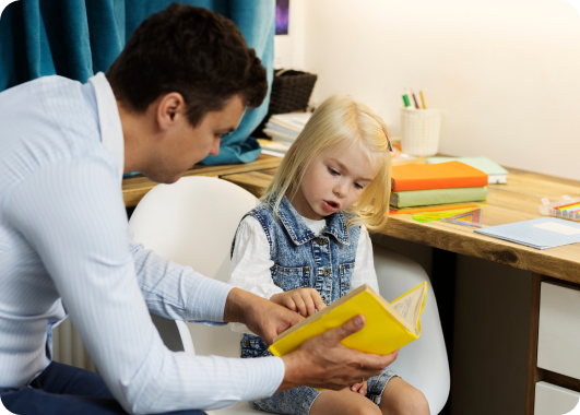 A psychologist pointing to a colorful children's book during a session with a young girl.