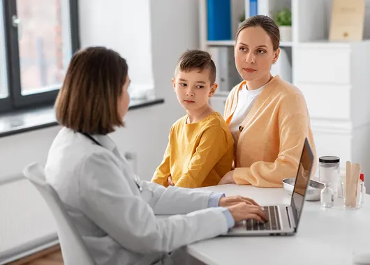 A therapist talking with a mother and her young son at a clinic desk.
