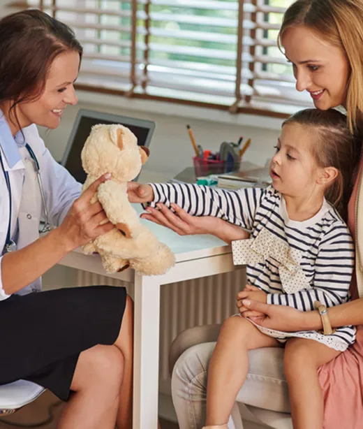 A pediatrician using a teddy bear to put a young patient at ease during an exam.